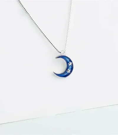 Pendentif en forme de lune bleue avec étoiles, suspendu à une chaîne fine.