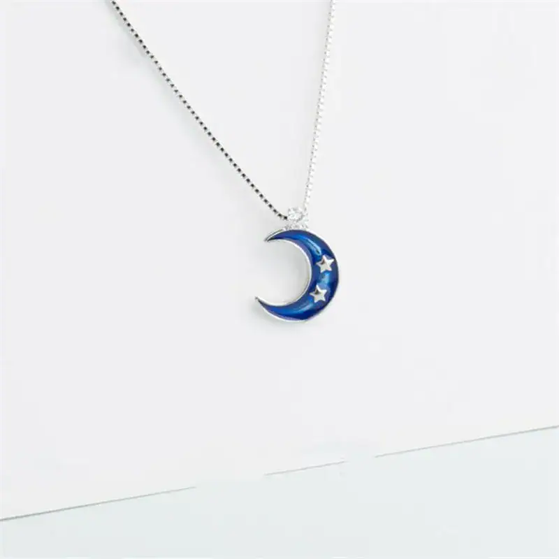 collier-croissant-de-lune-bleu-1 Pendentif en forme de lune bleue avec étoiles, suspendu à une chaîne fine.