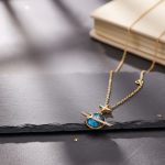 Collier fantaisie avec pendentif planète et étoile, inspiré de l'espace, en or et bleu, posé sur une surface sombre avec un livre en arrière-plan.