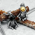 Pendentifs astronautes en métal avec boules de couleur dorée et noire, suspendus à une chaîne, inspirés de l'espace et de l'exploration spatiale.