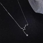 Collier délicat avec pendentif en forme de constellation étoile, en argent, suspendu à une fine chaîne, posé sur un fond noir avec un tissu en maille.