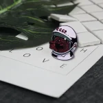 Poinçon en forme de tête de loup portant un casque spatial avec inscription "CCCP", posé sur une feuille avec des lettres "LOVE" et des pièces de jeu d'échecs en arrière-plan.