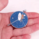 Une broche représentant une station spatiale avec antennes et panneaux solaires, idéale pour les amateurs d'astronomie et de décoration scientifique.