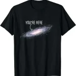 T-shirt galaxie avec texte "You're Here" en blanc sur fond noir, représentant une galaxie spirale avec un message humoristique et cosmique.