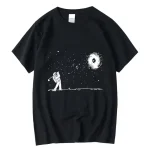 T-shirt noir avec un motif d'astronaute jouant dans l'espace, observant une galaxie et des étoiles, design minimaliste et artistique.