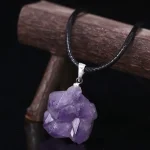 Pendentif en cristal d'améthyste brut suspendu à un cordon noir, idéal pour la décoration ou le port.