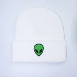 Casquette blanche avec logo d'alien vert et noir, style streetwear tendance.