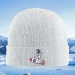 Casquette en laine blanche avec broderie d'un petit astronaute sur une fusée, idéale pour les amateurs de science et d'exploration spatiale.