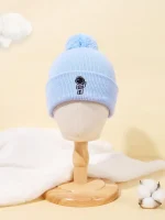 Bonnet en laine bleu clair avec un petit personnage scientifique brodé, orné d’un pompon en haut. Parfait pour les amateurs de science et de mode hivernale.