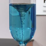 Pipette en liquide bleu versant dans un verre à pied, illustrant une expérience scientifique ou une démonstration de laboratoire.