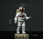 Figurine d'astronaute miniature avec casque doré, mesurant 22 cm de haut, 12 cm de large et 10 cm de profondeur, posée sur une base rocheuse, idéale pour décoration scientifique.