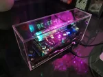 Panneau d'affichage électronique LED dans un boîtier transparent, affichant des chiffres lumineux en bleu et vert, avec des composants électroniques visibles à l'intérieur.
