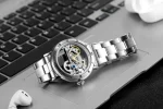 Montre mécanique avec mouvement visible, bracelet en acier inoxydable, posée sur un clavier d'ordinateur.