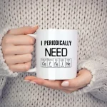 Tasse blanche avec message "I Periodically NEON" et symboles d'éléments chimiques, tenue par une personne en pull beige, sur fond neutre.
