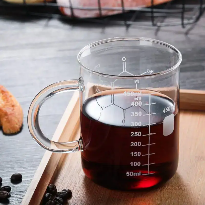 mug-molecule-cafeine-1 Tasse de laboratoire en verre contenant un liquide foncé, graduée pour mesurer précisément le volume, idéale pour expériences scientifiques ou décoration thématique.
