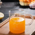 Verre de chimie en verre transparent rempli d'un liquide orange, posé sur une planche en bois, avec des fruits en arrière-plan.