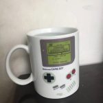 Mug en forme de console Game Boy avec écran affichant "Super Mario Land" et boutons colorés, idéal pour les fans de jeux vidéo rétro.
