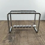 Pendulette de Newton en métal brillant avec six sphères suspendues, illustrant la conservation de l'énergie et la physique newtonienne.