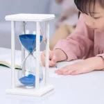 Horloge de sable avec cadre en bois blanc et sable bleu, utilisée comme objet éducatif ou décoration scientifique.