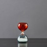 Balancier de sablier en verre rouge et transparent avec sable blanc.
