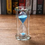 Sablier en verre avec sable bleu, symbole de la mesure du temps, idéal pour la décoration scientifique ou éducative.