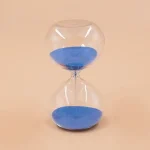 Sablier en verre transparent rempli de sable bleu, symbole du temps qui passe, idéal pour la décoration scientifique ou éducative.