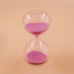 Sablier en verre transparent contenant du sable rose, symbole de temps et de patience, idéal pour la décoration scientifique ou éducative.
