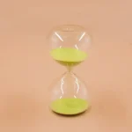 Sablier en verre transparent avec sable vert, symbole de temps et de patience, idéal pour la décoration scientifique ou comme objet de collection.