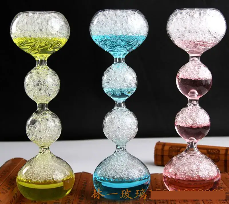 sablier-original-relaxant-1 Balançoire en verre coloré avec bulles d'air, composée de trois segments en forme de boule, chacun rempli de liquide coloré (jaune, bleu, rose) et de bulles d'air, sur fond noir.