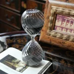 Sablier en verre transparent avec grains de sable noirs, décoration élégante et vintage pour un intérieur sophistiqué.