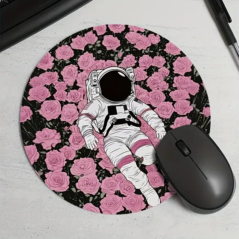 tapis-de-souris-astronaute-prairie-1 Vêtement d'astronaute illustré posé sur un tapis rond à motif de roses roses et noires, avec une souris d'ordinateur noire à côté.