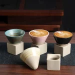 Trois tasses en céramique avec motifs colorés et design moderne, posées sur des supports en béton, sur une surface en bois, illustrant un objet de décoration scientifique.