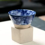 Petite tasse en céramique avec motif marbré bleu et blanc, posée sur un support en béton, idéale pour la décoration scientifique ou pour une utilisation pratique.