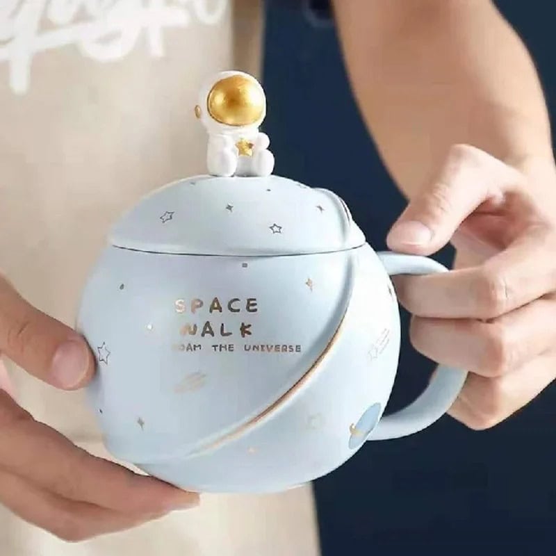 tasse-astronomie-1 Tasse en céramique avec motif spatial et figurine d'astronaute doré sur le couvercle, idéale pour la décoration ou la consommation de boissons inspirées de l'espace.