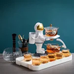 Décoration de thé originale avec un astronaute en céramique servant du thé chaud, entouré de tasses et accessoires de cuisine, sur fond bleu.