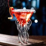Cocktail rouge dans un verre en forme de méduse avec tentacules en verre, garniture d'orange et glace, sur une surface en bois, ambiance nocturne et mystérieuse.