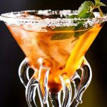 Verre à cocktail avec garniture de menthe et citron, décoré avec du sel sur le rebord, mettant en valeur une boisson colorée et rafraîchissante.