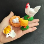 Poule en plastique blanc avec crête rouge, œufs blancs dans un nid orange, petite poule jaune sur un œuf cassé, figurines décoratives pour thème scientifique ou éducatif.