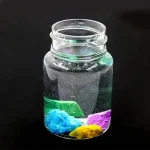 Vase en verre transparent contenant un liquide clair avec des substances colorées en dessous, créant un effet visuel scientifique et décoratif.