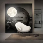 Lampe murale en forme de lune suspendue au-dessus d'un fauteuil moderne blanc dans un intérieur contemporain, avec étagère en arrière-plan.