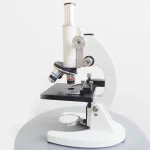 Microscope scientifique blanc pour observation précise en laboratoire ou à la maison. Idéal pour l'étude de petits objets, cellules ou micro-organismes avec une haute résolution.