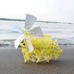 Véhicule scientifique miniature en plastique jaune avec hélice blanche, posé sur le sable près de la mer, illustrant un objet de décoration scientifique original et éducatif.