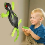 Jeune enfant souriant tenant une télécommande, interagissant avec un lézard robot lumineux fixé au mur.