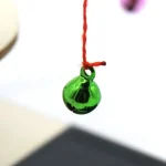 Boule de verre verte suspendue par un fil rouge, objet scientifique décoratif, mettant en valeur la transparence et la couleur vibrante du verre.