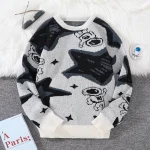 Pull en laine gris, noir et blanc avec motifs de personnages de dessins animés et étoiles, parfait pour un look casual et tendance.
