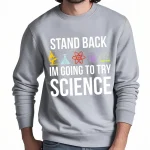 Sweatshirt gris avec message humoristique sur la science, "Stand back, I'm going to try science", avec icônes de laboratoire colorées.