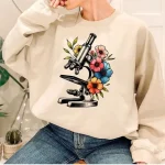 Sweatshirt avec motif de microscope entouré de fleurs colorées, parfait pour les amateurs de science et de décoration originale.