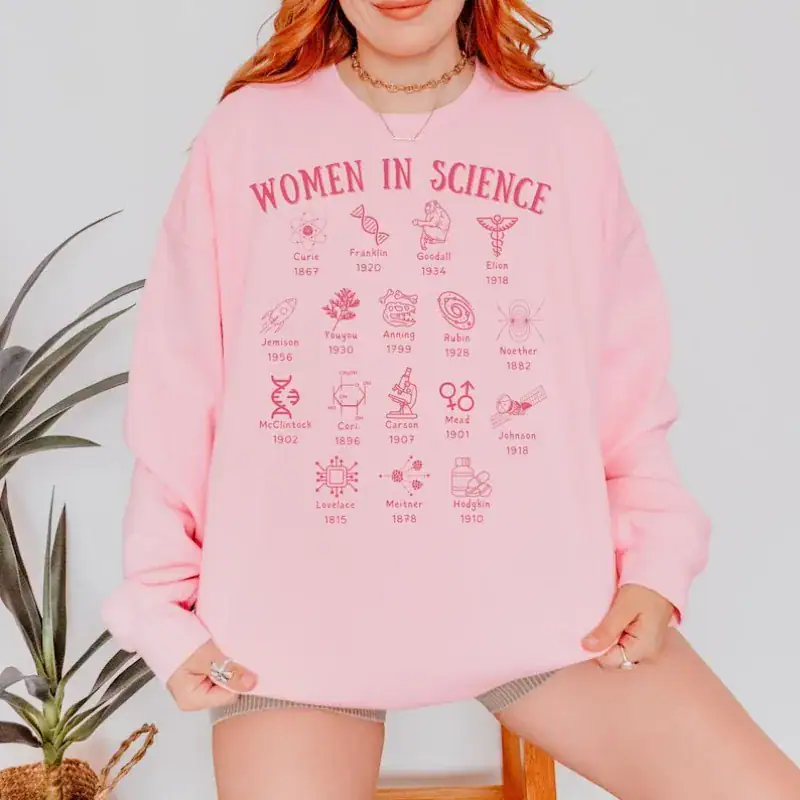 sweat-women-in-science-1 Sweatshirt rose avec motifs de femmes en science, illustrant l'engagement et la contribution des femmes dans le domaine scientifique. Parfait pour une tenue décontractée et engagée.