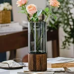 Fleurs roses dans un vase en verre avec socle en bois, décoration élégante et moderne pour intérieur.